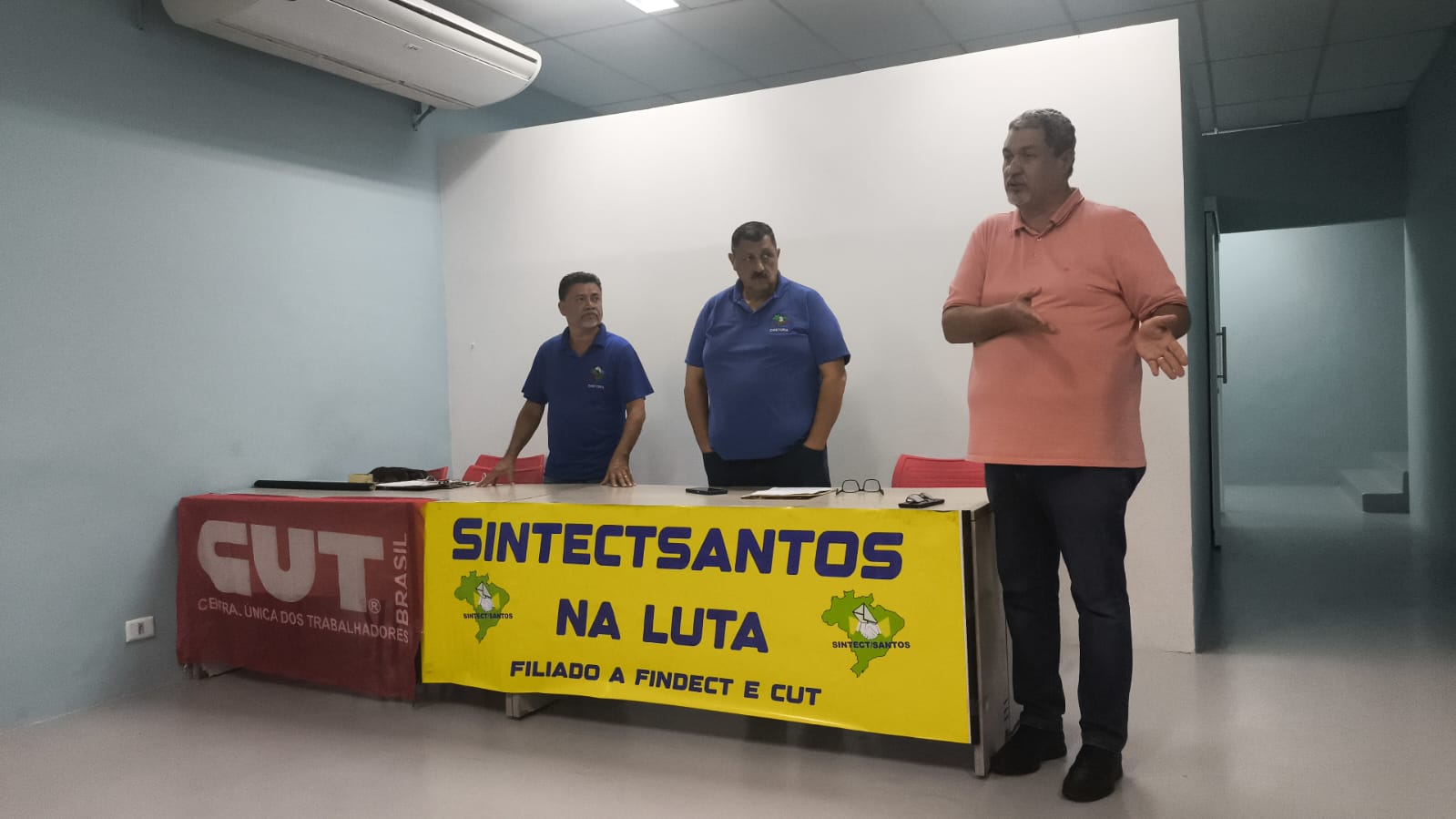 Membros da diretoria na mesa com banner SINTECTSANTOS NA LUTA